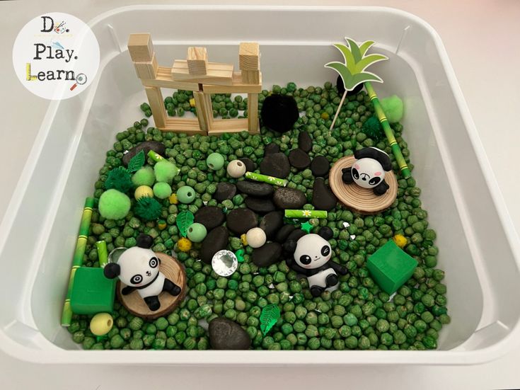 a plastic container filled with lots of green rocks and small pandas in the water