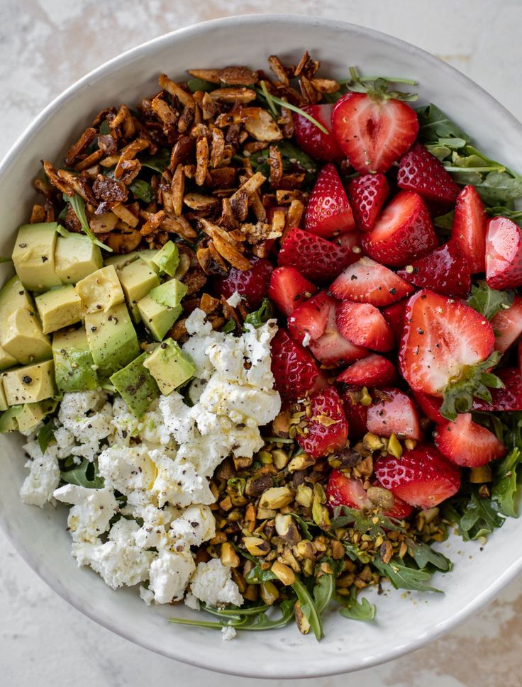 a white bowl filled with strawberries, avocado, nuts and feta cheese