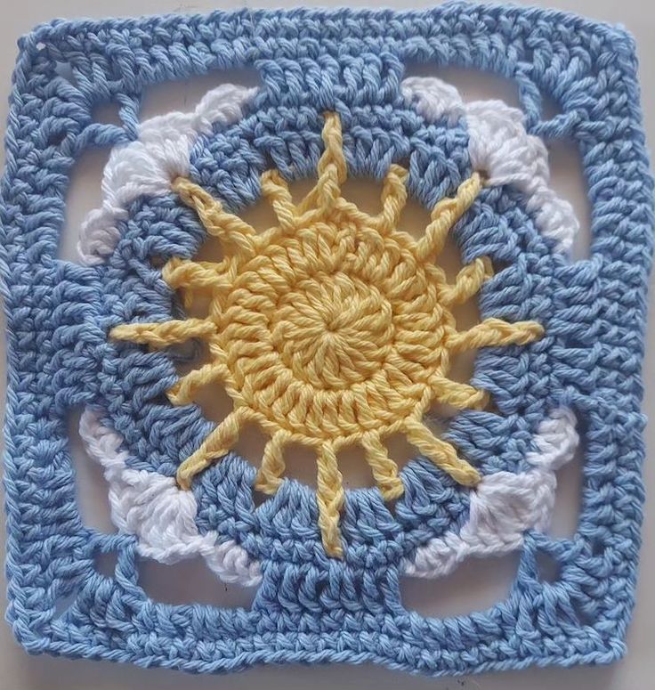 a crocheted square with a yellow sun on the center and white clouds around it