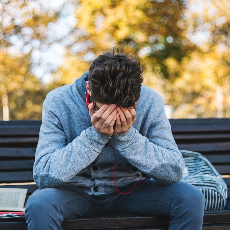 a man is sitting on a bench with his hands covering his face while listening to music