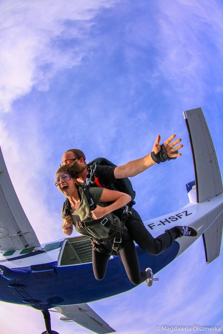 a man and woman are in the air with an airplane behind them, while another person is holding on to the wing