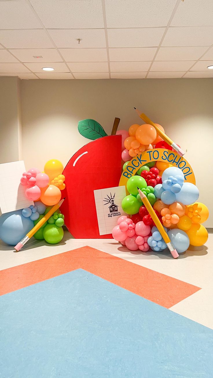 an apple surrounded by balloons and pencils on the floor in front of a bulletin board