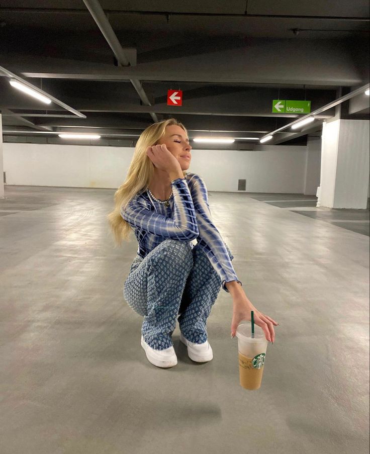 a woman sitting on the floor with a drink in her hand and looking up at something