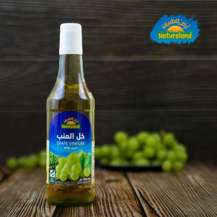 a bottle of green olive oil sitting on top of a wooden table next to grapes