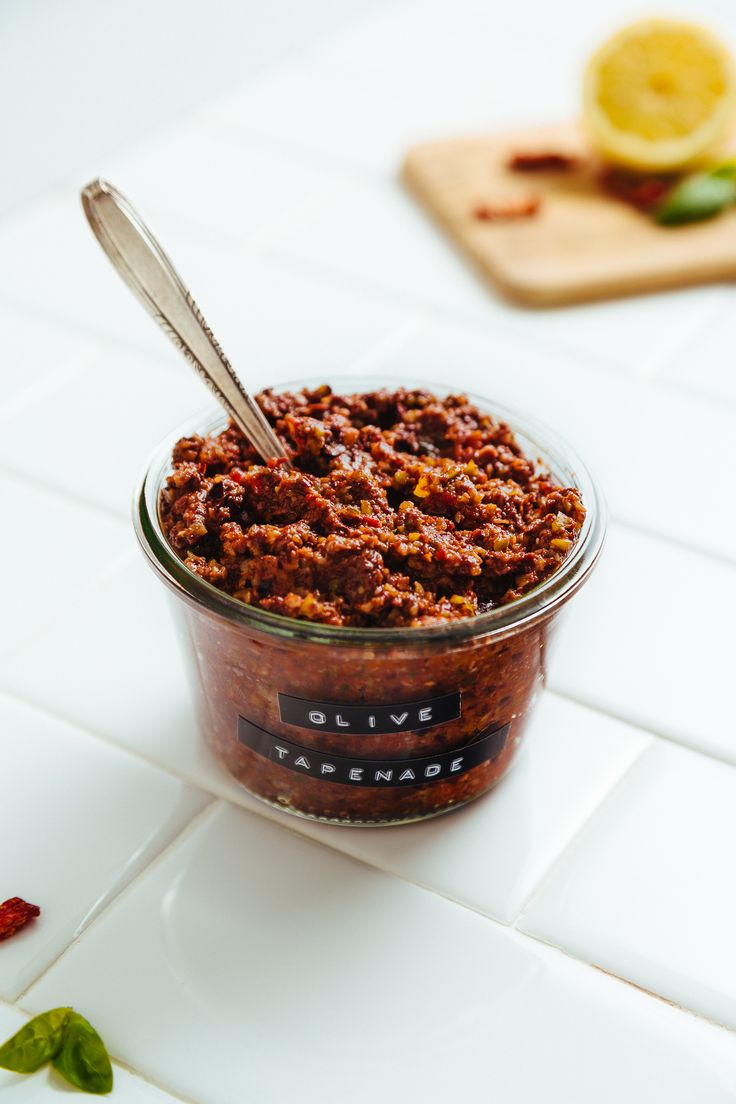 a glass jar filled with food sitting on top of a white tiled counter next to a cutting board