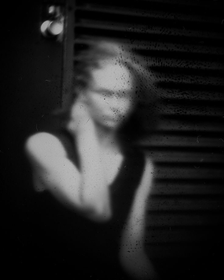 black and white photograph of a woman's face in front of a mirror with her hand on her shoulder