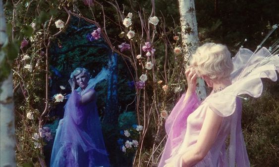 two women dressed as fairy tale characters in front of a floral arch with flowers and vines