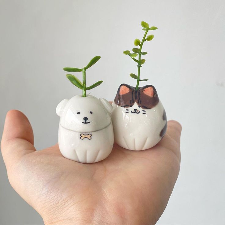 two small ceramic animals holding plants in their mouths