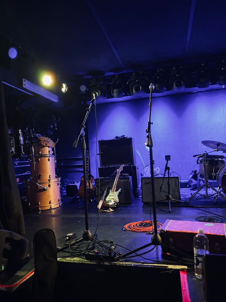 an empty stage with microphones, drums and other musical equipment on the floor at night