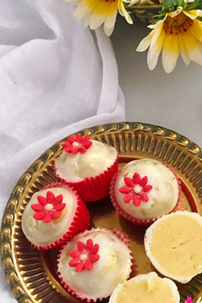 three cupcakes with red flowers on them sitting on a gold plate next to some daisies