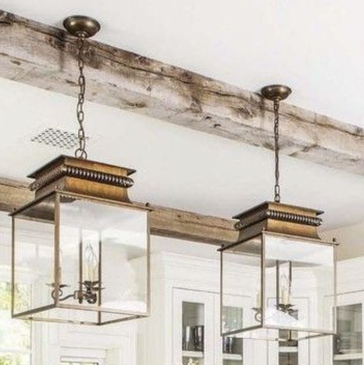 a kitchen with white cabinets and wooden beams on the ceiling is lit by three hanging lights