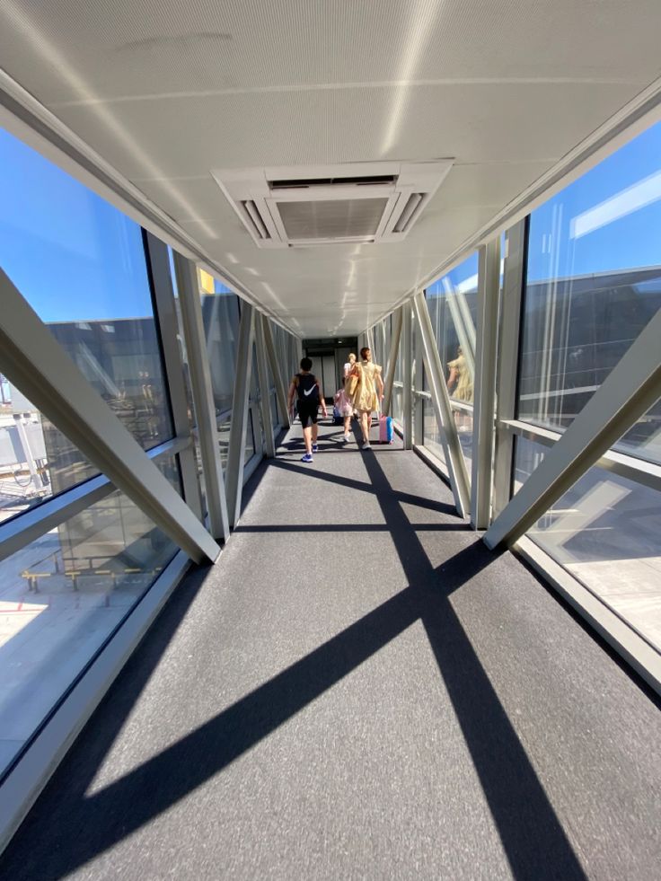 two people walking down a walkway in an office building with large windows on both sides