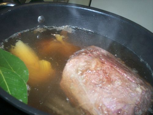 meat and vegetables are cooking in a pot on the stove top with green leafy garnishes