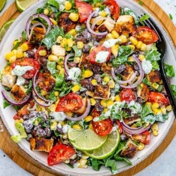 a salad with corn, tomatoes, onions and other vegetables on a wooden platter