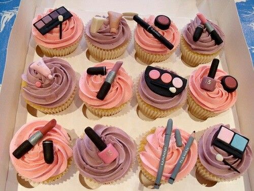 cupcakes decorated with pink frosting and various makeup items in a white box