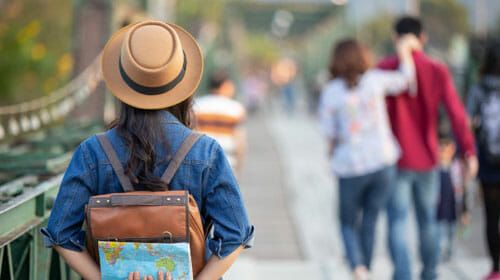 a woman with a backpack and hat walking down the street while holding a map in her hand