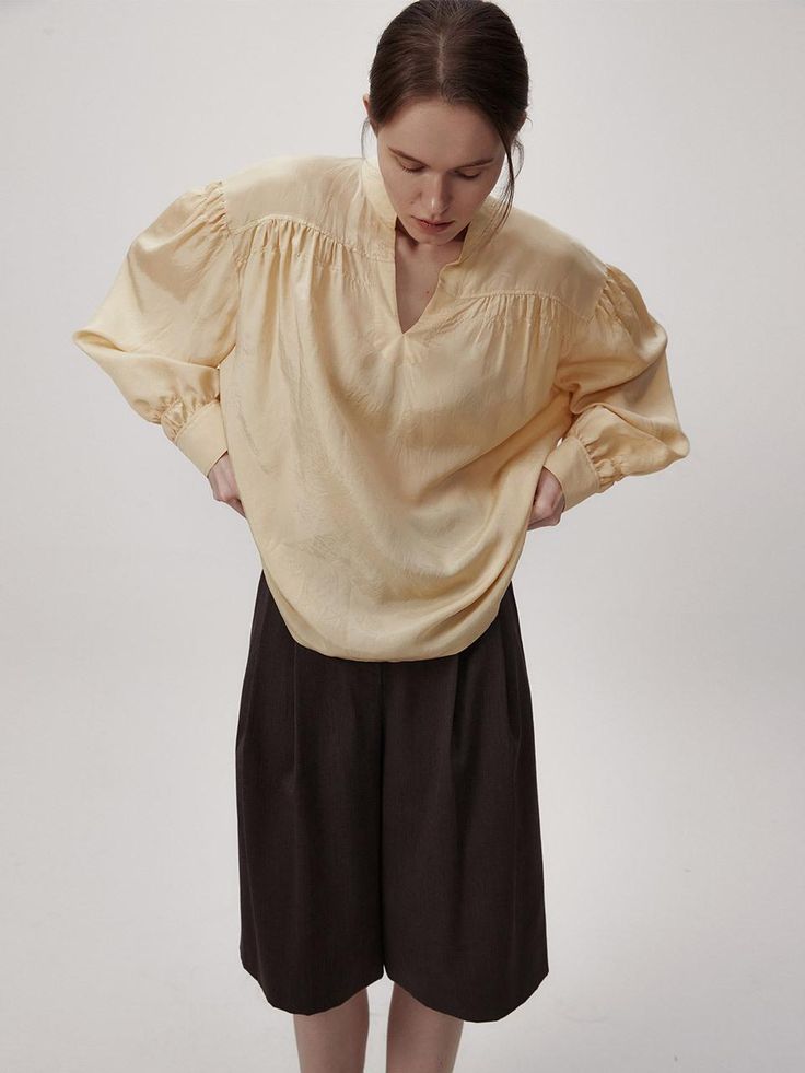 This product is a volume sleeve blouse that encapsulates modern elegance with its dramatic puff sleeves and airy silhouette. The design features a subtle V-neckline which adds a delicate touch, while the gathered details at the shoulders create an impactful volume, making it a statement piece for any wardrobe. - The blouse's voluminous sleeves are cinched at the wrists, balancing the proportions and adding sophistication to the overall design.- Made from a lightweight fabric, it provides a breezy feel and a comfortable fit for all-day wear.- The gathered shoulder detail and flowing silhouette offer a contemporary twist on the classic blouse.- Its relaxed and fluid design pairs effortlessly with both slim and wide-leg pants, making it a versatile choice for both casual and dressy occas Formal Top With Lantern Gathered Sleeves, Formal Blouse With Bishop And Gathered Sleeves, Chic Blouse With Bishop Blouson Sleeves, Classic Blouse With Bishop Sleeves, Silk Blouse With Blouson Sleeves And V-neck, Classic Blouse With Gathered Bishop Sleeves, Chic Puff Lantern Sleeve Top For Office, Elegant Blouse With Puff Gathered Sleeves, Office Blouse With Gathered Lantern Sleeves