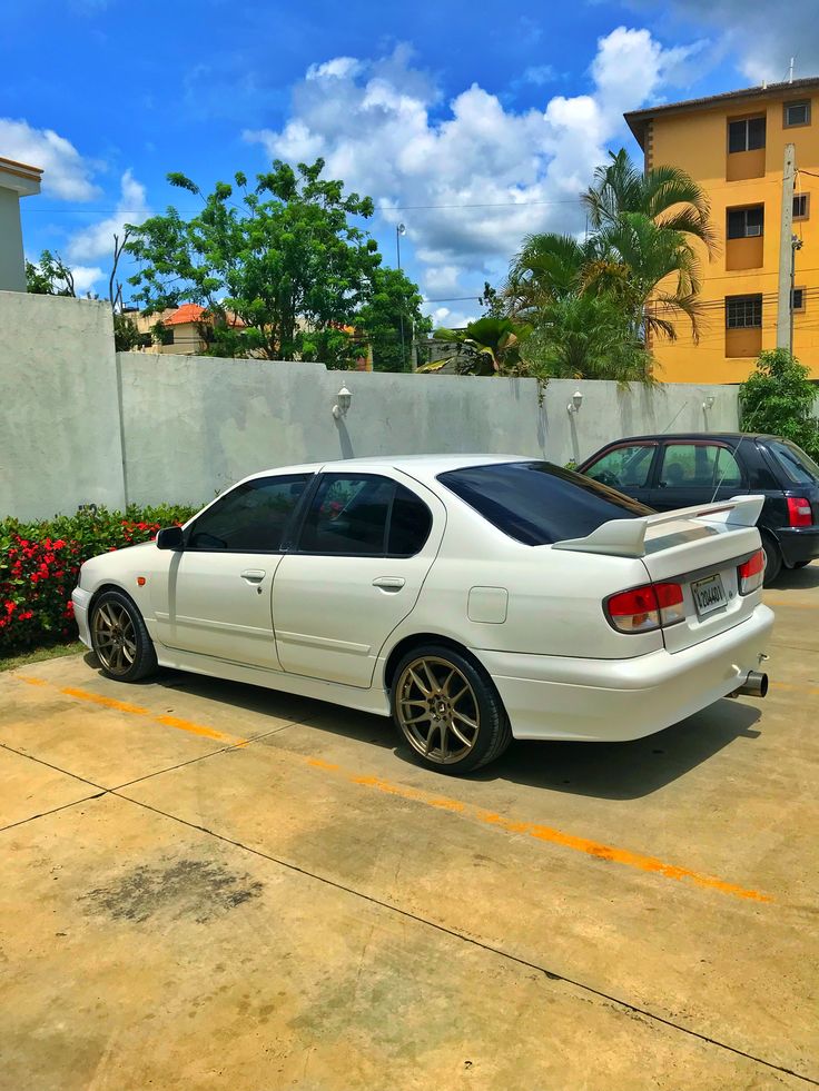 a white car parked in a parking lot next to a tall building with red flowers