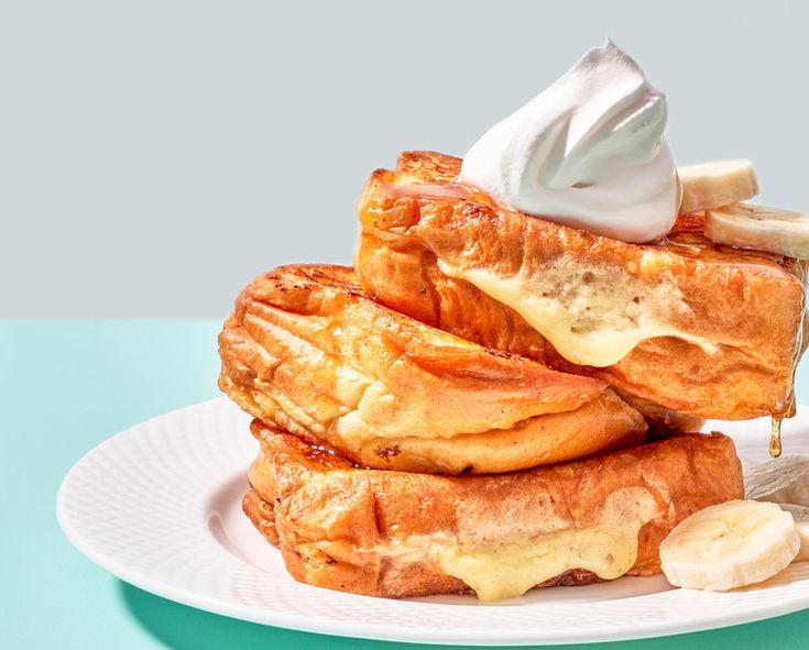 a stack of french toast on a plate with bananas and whipped cream in the middle