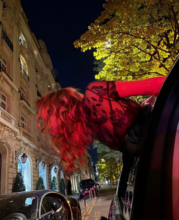 a woman with red hair leaning out the window of a car