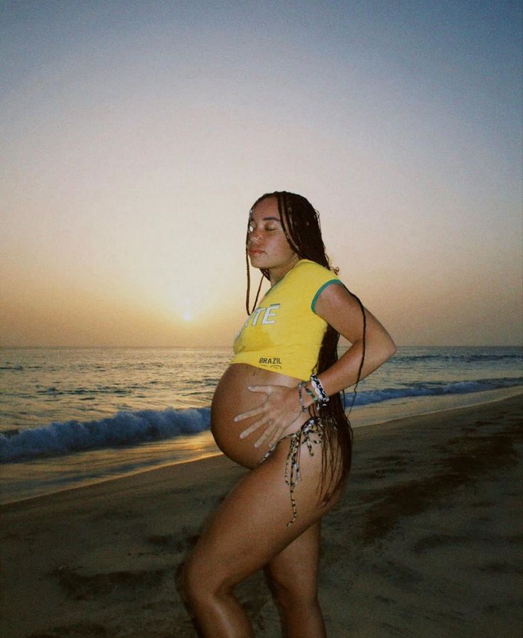 a pregnant woman standing on the beach at sunset with her belly covered in sand and water