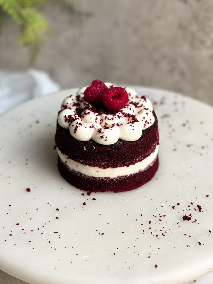 a red velvet cake with white frosting and raspberries on top is sitting on a plate