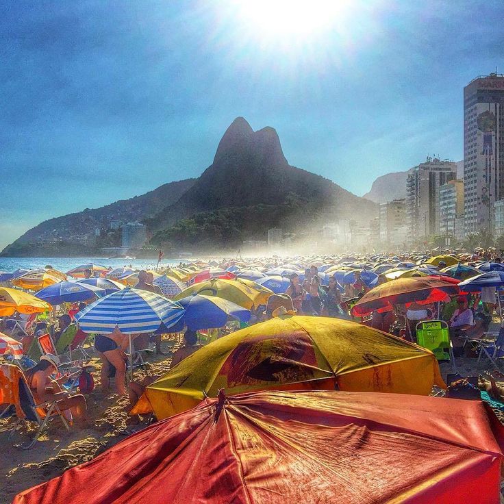 many colorful umbrellas are on the beach with buildings and mountains in the back ground