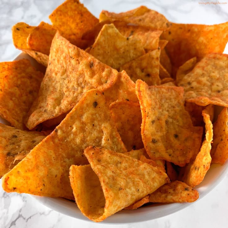 a white bowl filled with tortilla chips on top of a marble countertop