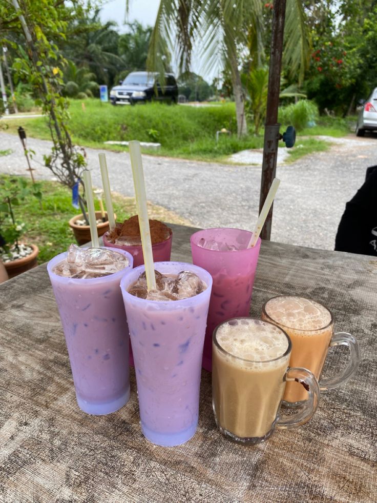 there are three drinks on the table with straws in each cup and one is purple