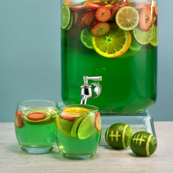 a pitcher filled with green liquid next to two glasses full of water and sliced fruit