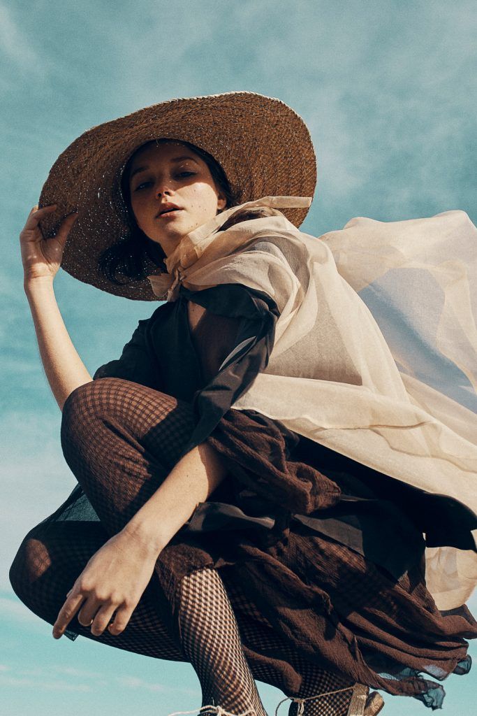 a woman in a hat and dress sitting on top of a skateboard