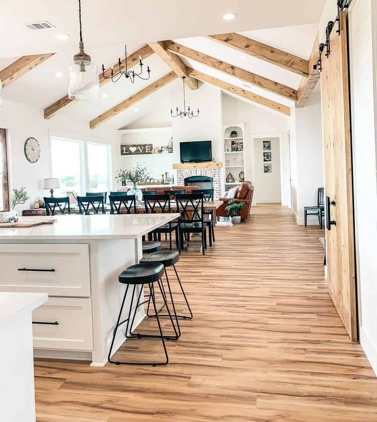 a large open kitchen and dining room with wood beams on the ceiling, hardwood flooring