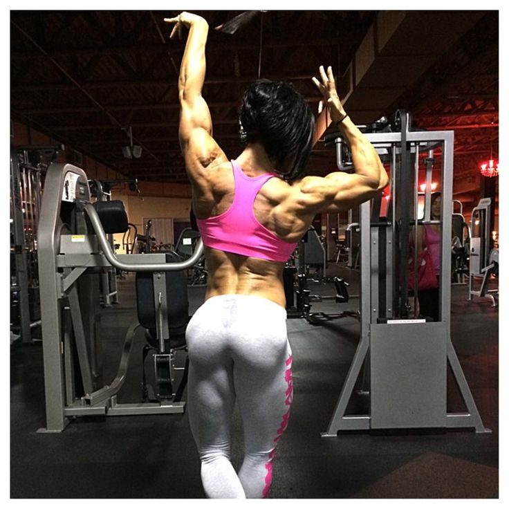 a woman in pink top and white shorts working out at a gym with her back turned to the camera