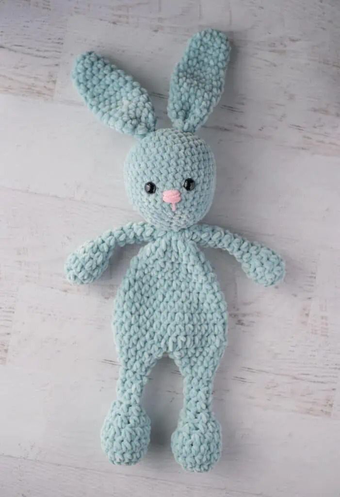 a crocheted blue bunny stuffed animal on a white wooden surface with the eyes closed