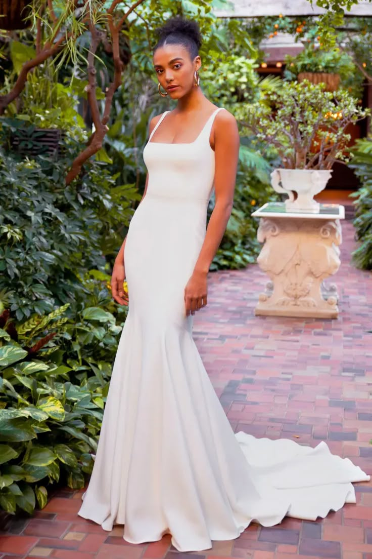 a woman in a white wedding dress standing on a brick walkway surrounded by greenery