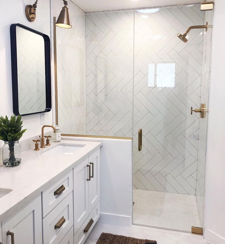 a white bathroom with gold accents and marble counter tops is pictured in this image, there are two mirrors on the wall next to the shower