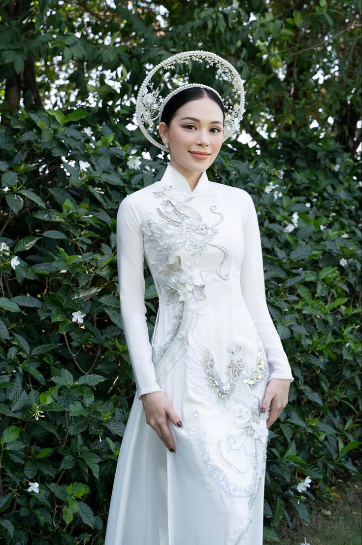 a woman in a white dress and headpiece standing next to some bushes wearing a tiara