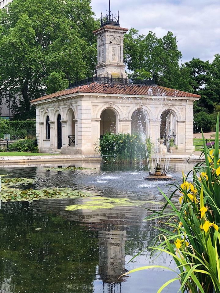 a building with a fountain in front of it and flowers around the pond area on either side