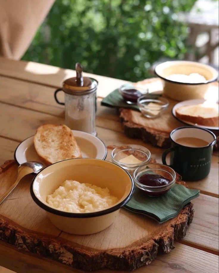 a table topped with bowls of food next to cups of coffee and saucers on top of a wooden table