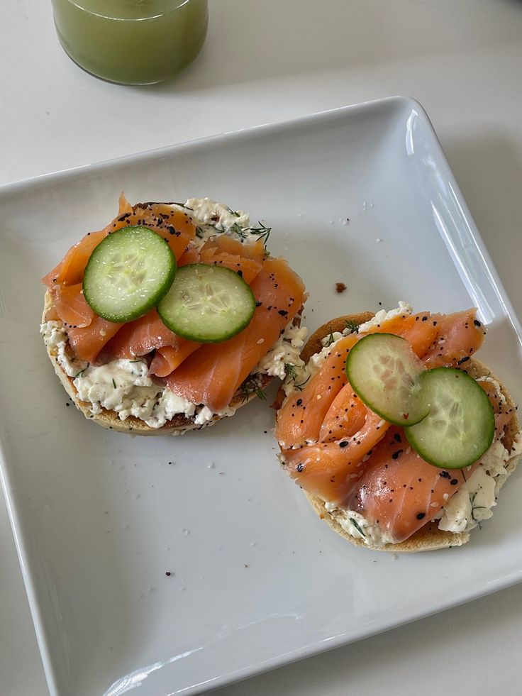 two small sandwiches with cucumbers and cheese on them sitting on a white plate