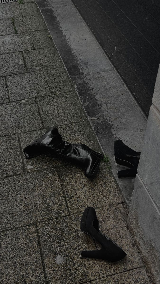 a pair of black high heeled shoes laying on the ground next to a wall