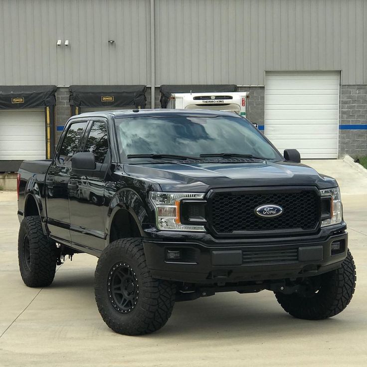 a black pickup truck parked in front of a building with large tires on it's tires