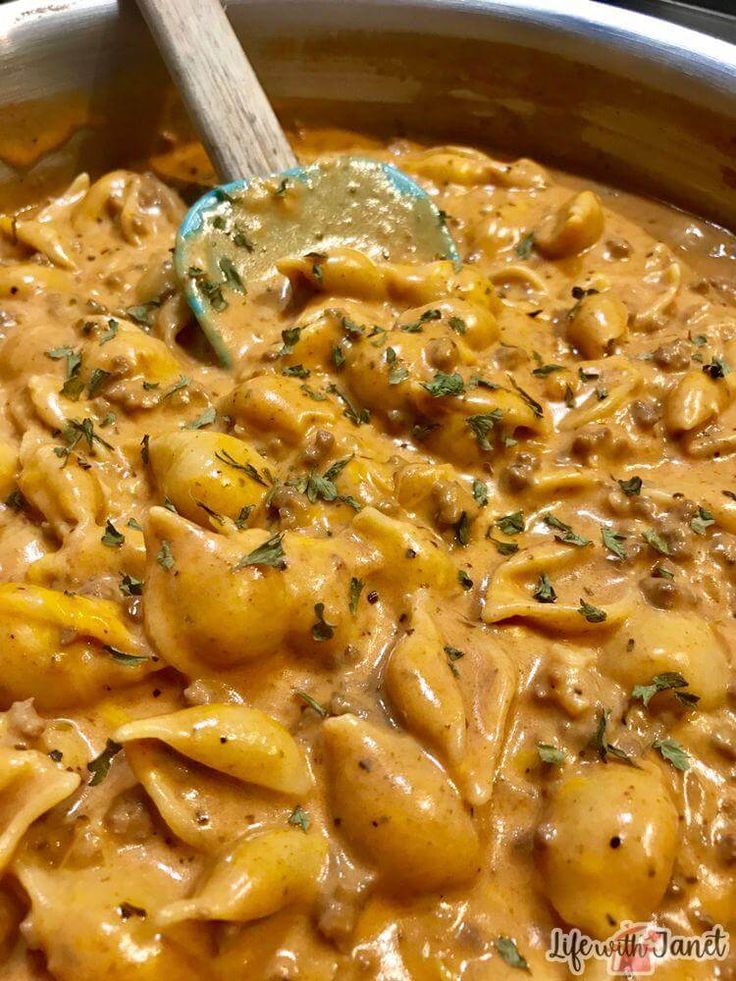 a pot filled with pasta and cheese covered in gravy next to a wooden spoon