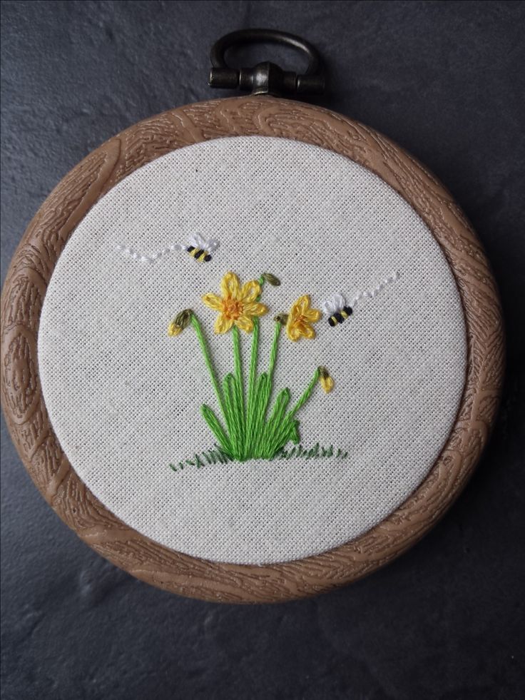 an embroidery project with daffodils and bees in the grass on a wooden hoop