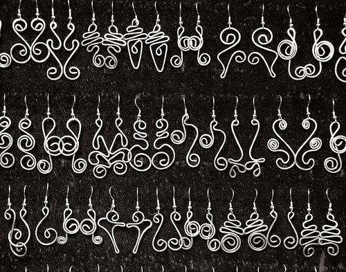 several pairs of earrings hanging from hooks on a black background with white swirls and hearts