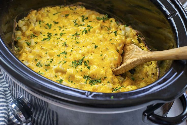 a crock pot filled with macaroni and cheese next to a wooden spoon