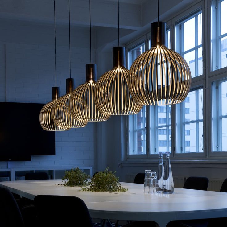 a dining room table with four hanging lights above it and vases on the table