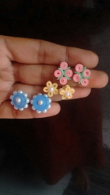 a person holding three different colored flowers in their hand with pearls on the petals and beads attached to them