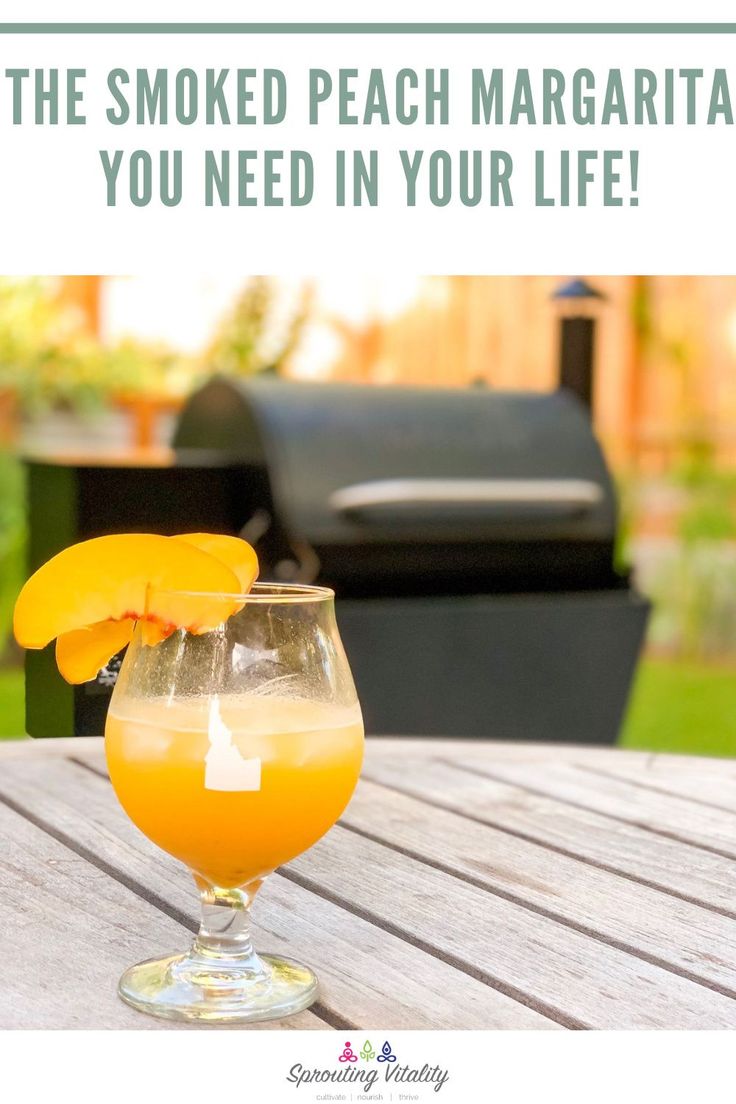 a glass filled with orange juice sitting on top of a wooden table next to a bbq