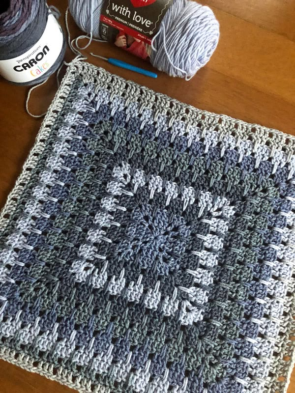 a crocheted square with yarn and scissors on the table next to it is a ball of thread